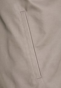 Tessuto grigio chiaro con una tasca rettangolare con cuciture a contrasto, che enfatizza una superficie liscia e un design minimalista.