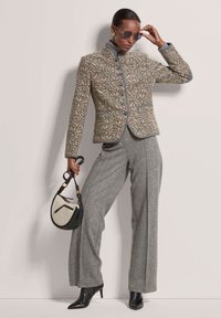 Wollen blend jasje met een geometrisch patroon in beige en grijs, gecombineerd met grijze uitlopende broek en een zwarte handtas met een crèmekleurig accent.