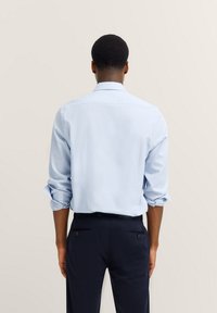 Helles blaues Hemd mit langen Ärmeln, die an den Manschetten hochgerollt sind. Verfügt über einen schlichten Kragen und einen glatten, strukturierten Stoff. Lässiges Design.