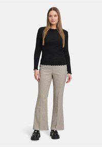 Zwarte langemouwen top met een gegolfde zoom en manchetten, gecombineerd met een geruite flared broek en chunky zwarte plateau schoenen.