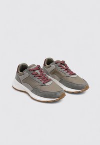 Un paio di sneaker basse e casual in grigio e taupe con lacci bordeaux e suole in gomma bianca su uno sfondo chiaro.