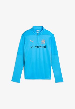 Camiseta deportiva de manga larga azul claro con cremallera hasta el pecho, logo de Puma, emblema del Olympique de Marseille y patrocinador Randstad en la parte delantera.