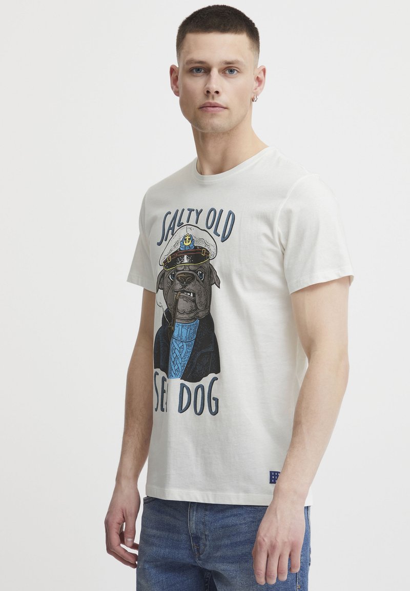 Cremefarvet bomulds T-shirt med et grafisk motiv af en hund i kaptajnshat, med blå accenter og teksten "SALTY OLD SEA DOG." Kortærmet.