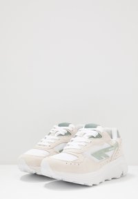 White sneakers with green accents, featuring a combination of suede and mesh materials, a cushioned sole, and lace-up design.