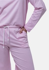Rosa lounge-set i mjuk bomull med avslappnad passform. Har långa ärmar, dragsko i midjan och sidofickor. Slät textur och minimalistisk design.
