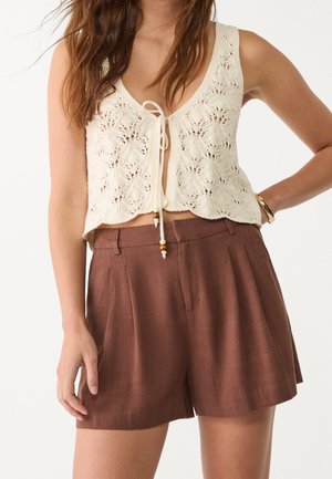 Krémový pletený crop top s květinovým vzorem a zavazováním, spárovaný s hnědými šortkami s vysokým pasem, které mají sklady a texturovaný povrch.