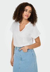 Biała lniana bluzka z krótkim rękawem, z dekoltem w serek i podwiniętymi mankietami, w połączeniu z jasnobłękitną spódnicą jeansową o wysokim stanie, z zamkiem na guziki z przodu.