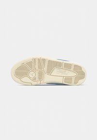 Semelle de chaussure en caoutchouc blanc texturé, présentant un motif en chevrons et un détail de logo circulaire. La couleur est crème avec des accents bleus.