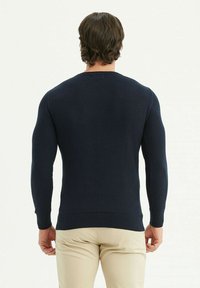 Pull en tricot bleu marine avec des manches longues, poignets et ourlet à côtes, présentant un col rond et une coupe ajustée.