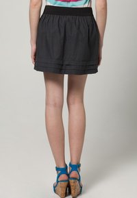 Falda negra plisada con cintura fruncida, que presenta una textura suave. Se lleva con sandalias de cuña azules con tiras y plataforma de corcho.