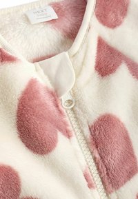 Kuschelige Zip-Jacke in Creme mit großen rosa Punkten. Merkmale sind eine dicke Textur, weicher Stoff und ein weißer Reißverschluss.