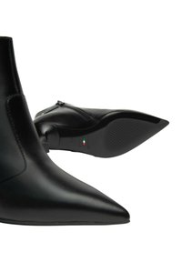 Stivaletti neri alla caviglia con punta affusolata, in morbida pelle, con zip laterale e suola in gomma testurizzata. Logo decorativo sul tacco.