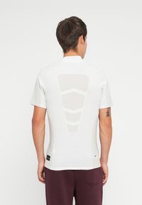 White athletic t-shirt featuring a cutout design on the back, short sleeves, and a slim fit. Soft texture with minimal branding at the hem.