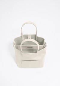 Borsa a tracolla beige con due manici, texture liscia, tasca frontale con logo impressionato e scomparto interno removibile. L'interno presenta una tasca piatta.