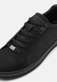 Tenis cu un finisaj mat neted, panou lateral texturat, vârf rotunjit, șireturi plate negre și un accent subtil al logo-ului.