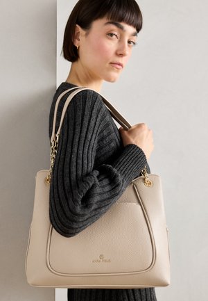 Beige leren handtas met een gestructureerde afwerking, voorzien van gouden accenten en een gestructureerde vorm. Draagt men met een donkergrijze geribde trui.