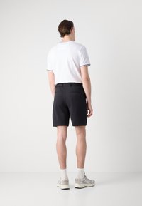 Cămașă polo albă cu mânecă scurtă și margini negre, combinată cu pantaloni scurți negri până la genunchi. Modelul poartă adidași gri și șosete albe.
