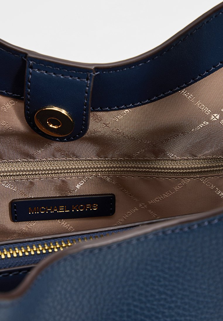 Intérieur d'un sac à main en cuir marine avec une fermeture éclair dorée, doublure beige et une étiquette noire avec "MICHAEL KORS". Il possède une fermeture à bouton.