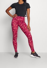 Zwart cropped T-shirt gecombineerd met hooggetailleerde legging met roze luipaardprint. Model draagt zwarte sportschoenen.