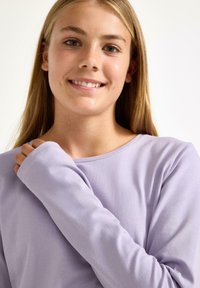 Langærmet lavendelskjorte med en blød tekstur og en rund halsudskæring. Har let oversized ærmer og en afslappet pasform.