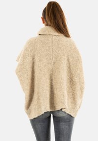 Beige oversized poncho met een textuurafwerking, open voorkant en brede kraag, met een losse pasvorm die over de schouders hangt.