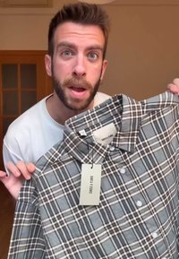 Chemise à carreaux gris et blancs avec un col boutonné, équipée d'une étiquette et de plusieurs boutons. Le tissu semble doux avec une coupe standard.