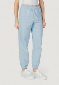 Světle modré volné tepláky s elastickým pasem a manžetami, s hladkým povrchem. Kombinováno s bílými teniskami.