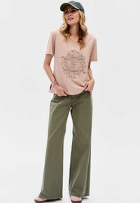 Roze v-hals t-shirt met een grafisch ontwerp van bloemen en boomringen, gecombineerd met olijfgroene wijde broek. Textuurstof en een relaxte pasvorm.