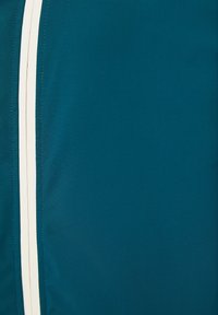 Turkos tyg med en slät textur och två vertikala vita ränder, prydligt dekorerad med fina sömmar längs kanterna.