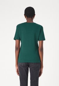 Grön bomullströja med rund hals och korta ärmar, med en figurnära passform och ribbad textur, tillsammans med svarta jeans.