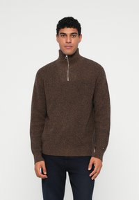 Brun strikket pullover sweater med høj krave og halvlynlås. Har et tekstureret mønster og en diskret logoaccent på ærmet.