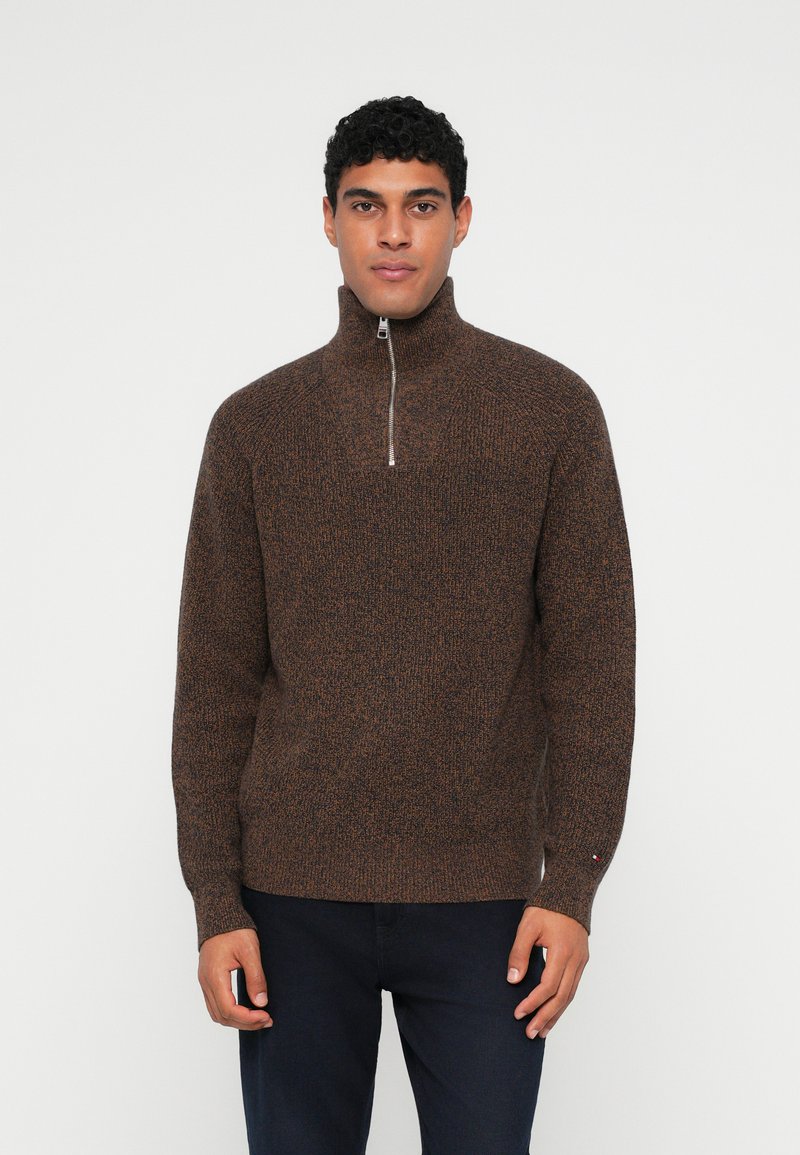 Brun strikket pullover sweater med høj krave og halvlynlås. Har et tekstureret mønster og en diskret logoaccent på ærmet.