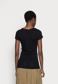 Czarny t-shirt z krótkim rękawem i okrągłym dekoltem, o subtelnej fakturze, zestawiony ze spódnicą plisowaną w kolorze metalicznego złota.