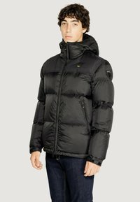 Giacca a vento nera imbottita con colletto alto e cappuccio. Presenta chiusura con zip, polsini elasticizzati e una patch del logo sulla spalla. Finitura liscia e lucida.