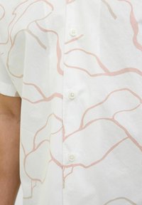Camisa blanca de botones con patrones abstractos en tonos blush y beige. Confeccionada en tela ligera, cuenta con un collar clásico y cierre de botones.