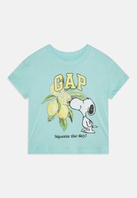 Piparmētru zaļa īsais piedurkņu T-krekls, izgatavots no kokvilnas. Tam ir Snoopy tēls, citroni un "GAP" teksts dzeltenā un melnā krāsā.