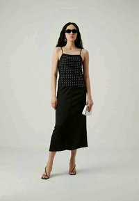 Zwarte tanktop met zilveren studs, gecombineerd met een zwarte midirok. Accessoires omvatten een slanke zwarte zonnebril en een kleine zilveren clutch.
