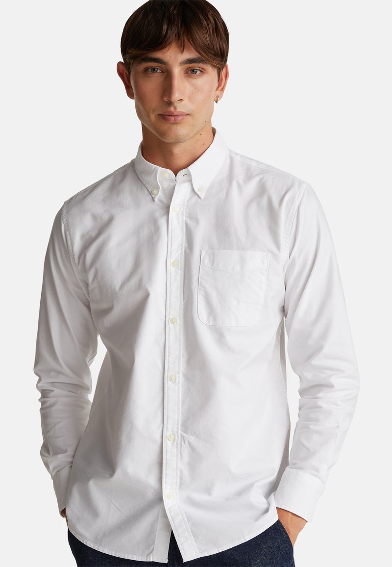 Camicia bianca button-up realizzata in tessuto di cotone, presenta un colletto classico, maniche lunghe e una tasca sul petto. Texture liscia, design aderente.