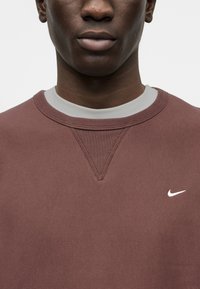 Μπορντό φούτερ από μαλακό ύφασμα, διαθέτει ριμπ λαιμόκοψη, λεπτομέρεια με ραφή σχήματος V και μικρό λευκό λογότυπο Nike στο αριστερό στήθος.