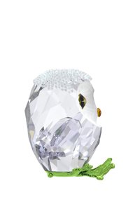 Kryštálová figúrka sovy s fazetovaným telom, bielymi akcentmi, čiernymi očami a zelenou podstavou pripomínajúcou listy, so štruktúrovanou korunou.
