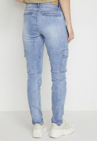 Vaaleansiniset farkkukangasta valmistetut cargo-housut, joissa on tiivis malli, kaksi sivutaskua, takataskut ja ommellut yksityiskohdat. Silkkinen kangastuntuma ja hengittävä materiaali.