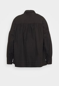 Camisa de algodão preta com pala nas costas, detalhes franzidos, mangas longas e punhos com botão. Textura suave e design estruturado.