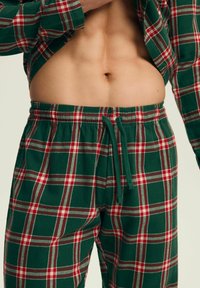 Zielone flanelowe spodnie do spania w kratę z białymi i czerwonymi wzorami, elastyczną talią z troczkiem oraz miękkiego bawełnianego materiału.