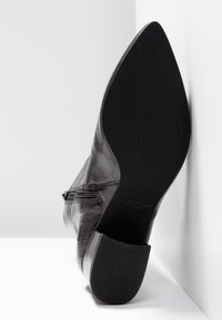 Bottine en cuir noir avec un bout pointu, une texture lisse et un talon moyen carré. Fermeture éclair latérale pour plus de praticité.