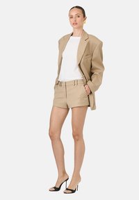 Beige oversize blejzer, biele tričko a strihané béžové kraťasy. Čierne sandále na vysokom opätku. Hladká tkanina, štruktúrovaný dizajn a ležérny strih.