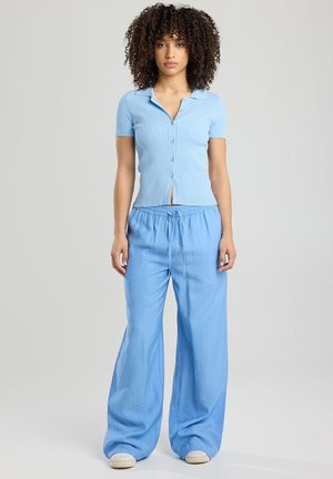 Camisa de punto acanalado de color azul claro con cuello y mangas cortas, combinada con pantalones holgados de tiro elástico de color azul claro, ambos en una textura suave.