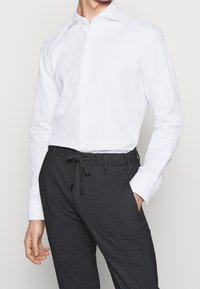 Biała koszula z długim rękawem z kołnierzykiem zapinanym na guziki, w połączeniu z ciemnoszarymi spodniami w kratę, które mają elastyczny pas i sznurek do regulacji.