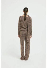 Pullover- und Hose-Set aus lila und beigem Strickstoff, mit lockerer Passform und einem über die Schulter drapierten Schal. Sanfte Textur.