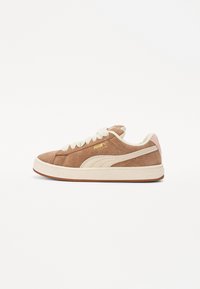 Brown suede sneaker with white laces, cream accents, and textured rubber sole. Features a pink heel and gold logo detail on the side.
