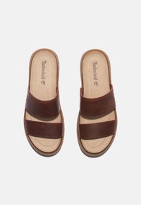 Sandali slide in pelle marrone con due ampie cinghie, soletta imbottita e suola texturizzata per una maggiore aderenza. Logo Timberland impresso sulla soletta.
